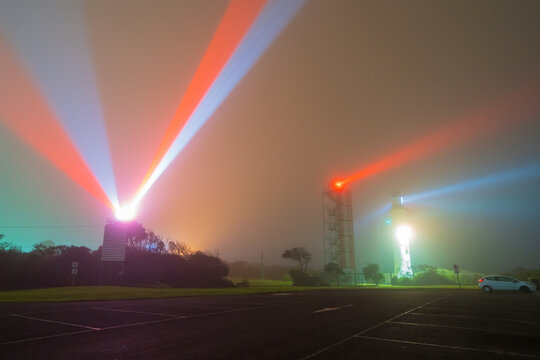 Beams of light from a lighthouse and beacon tower on a dark foggy night