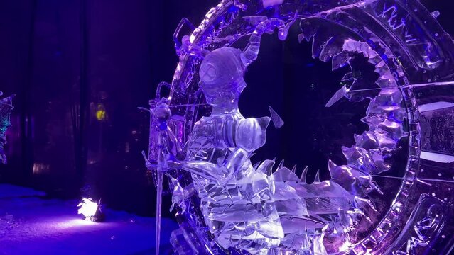 Incredible carved ice sculptures displayed in an interior hall of a pavilion illuminated with blue and purple lights.