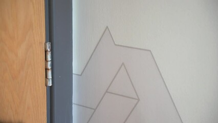 Workman installing vinyl wall graphic on to wall for client with geometric design using squeegee applicator in office space