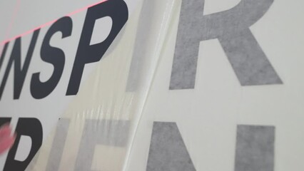 Close up of professional vinyl installer peeling off the excess protective cover to reveal the install wall graphic design wording on the wall from close up wide angle turning