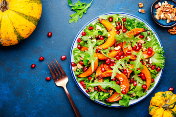 Healthy eating pumpkin salad with baked sweet pumpkin, lettuce, arugula, pomegranate seeds and nuts. Comfort food. Blue background. Top view