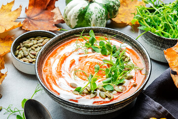 Pumpkin soup with seeds, cream and green pea sprouts. Winter or autumn healthy slow food. Soup bowl on gray table background. Top view
