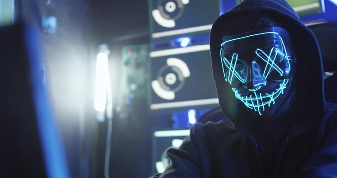 A hacker wearing a mask to cover his face is using computer to hack data to get ransom from victims.