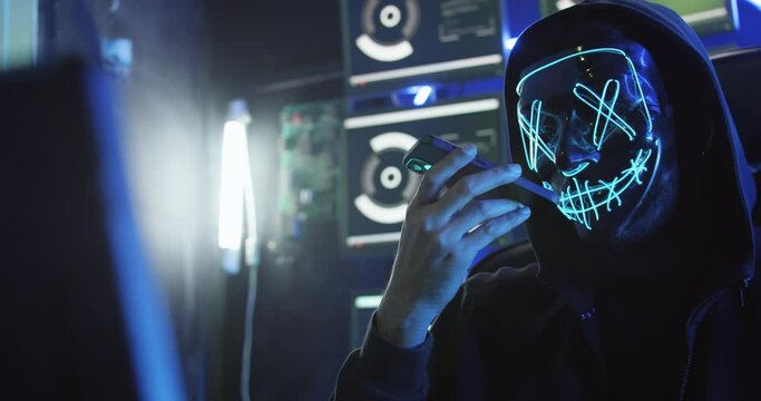 A hacker wearing a mask to cover his face is using computer to hack data to get ransom from victims.