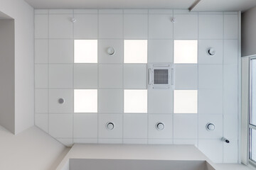 cassette stretched or suspended ceiling with square halogen spots lamps and drywall construction with fire alarm and ventilation in empty room in house or office. Looking up view - obrazy, fototapety, plakaty