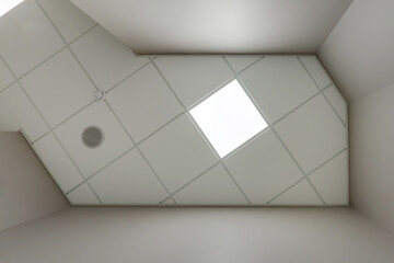 cassette stretched or suspended ceiling with square halogen spots lamps and drywall construction with fire alarm and ventilation in empty room in house or office. Looking up view - obrazy, fototapety, plakaty