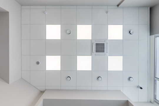 cassette stretched or suspended ceiling with square halogen spots lamps and drywall construction with fire alarm and ventilation in empty room in house or office. Looking up view - Powered by Adobe