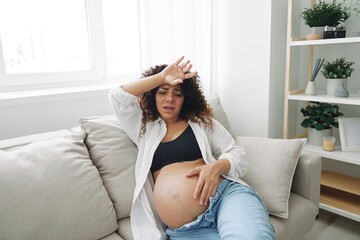 Pregnant woman headache lies at home on the couch fatigue and heaviness in the last month of pregnancy before childbirth, motherhood difficulties