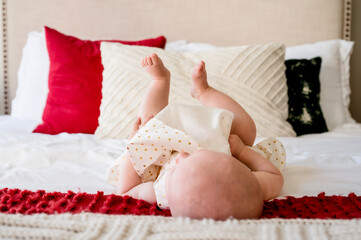 Baby laying on bed with feet in the hair, red green and white pillows and headboard in background