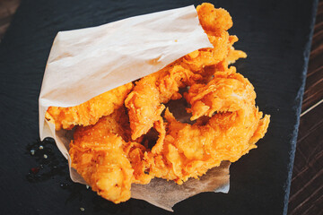 meat strips in a paper bag on a black tray. strips of meat fried in breading. 