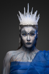 Studio shot of winter queen with blue cape and ice crown isolated on gray.