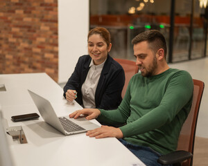 Caucasian bearded man and red-haired woman work in a modern coworking space. Colleagues discuss work.