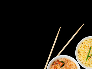 Delicious asian curly noodles and funchose salad in white bowls with wood sticks on black background. Selective focus. Asian food concept