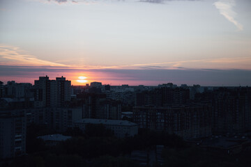 Fototapeta premium Sunset signals about upcoming night and illuminates high-rise city buildings. Streets become darker and trees silhouettes surround residential area