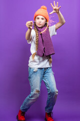 One Expressive Winsome Caucasian Girl in Coral Winter Warm Hat and Violet Knitted Scarf Having Fun With Vivid Bright Burning Bengal Light Fireworks Over Purple Background.