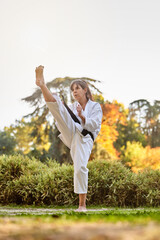 Fighter woman in kimono and black belt standing in karate position outdoors in nature. Sports and martial arts concept. © JoseIMartin