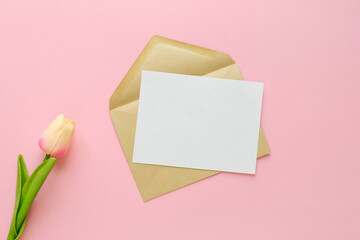 Craft envelope for letters with a blank sheet. Flat lay with a message and a tulip on a pink background