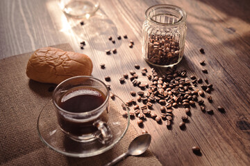 Hot coffee in a clear coffee cup and coffee beans on old wooden in a warm light.