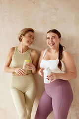 Smiling Woman Talking After Yoga. Female Friends Laughing And Holding Detox Drinks After Yoga...