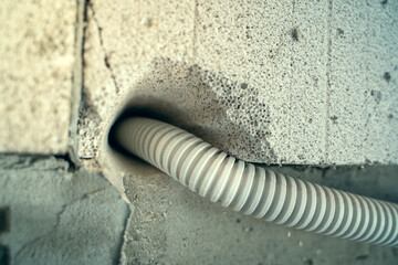 The wire in a protective plastic corrugated pipe is laid through the wall through a hole in the aerated concrete brick. Conducting electricity to the house. Drilled hole in gas block