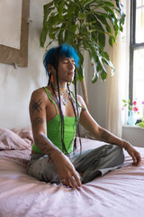 indigenous non-binary artist with blue hair meditating on bed