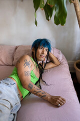 indigenous non-binary artist with blue hair and braids relaxing on bed