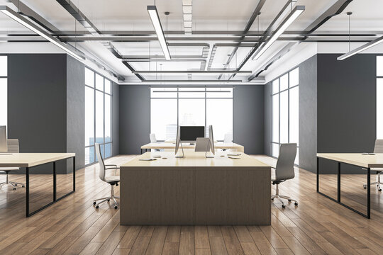 Side view on sunlit huge workspace table with modern computers on glossy wooden floor in stylish coworking office with loft ceiling lamps and dark walls background. 3D rendering