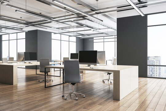 Perspective view on sunlit stylish open space office with modern computers on light tables on wooden floor, loft ceiling lamps and city view background from panoramic windows. 3D rendering