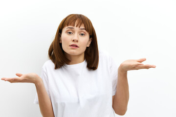 a pleasant, beautiful, attractive woman stands on a white background in a white T-shirt and looking at the camera, she spreads her arms in surprise to the sides