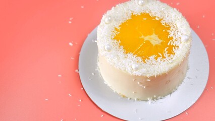 Cake with orange and coconut shavings spun on a pink background.