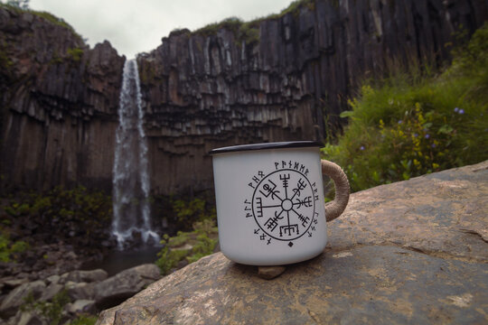 Close up mug on rock against waterfall concept photo. Travel adventure. Front view photography with steep cliffs on background. High quality picture for wallpaper, travel blog, magazine, article