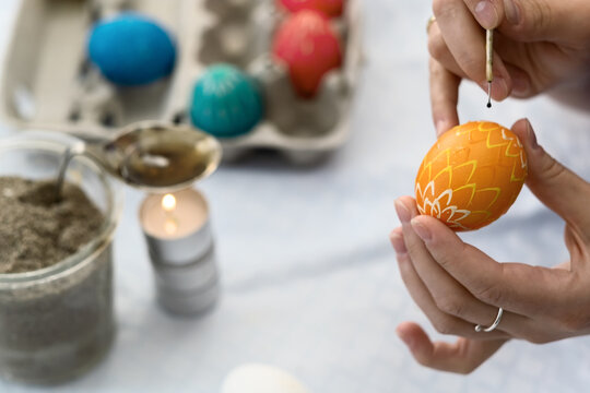 Female hands paint a yellow Easter egg with pattern according to Sorbian tradition with a needle head and melted candle wax
