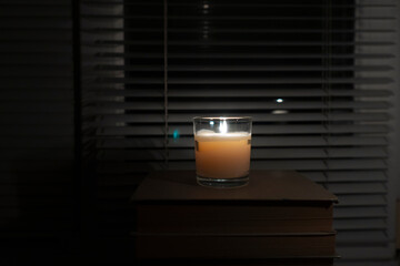 A candle with a glass cup stands in a dark empty room by the window