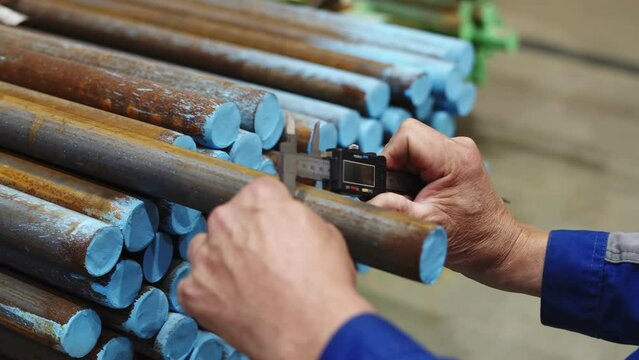 a worker in a blue uniform measures the diameter of a metal rod with a caliper in the workshop of a manufacturing enterprise, factory, close-up