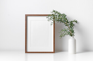 Wooden portrait frame mockup in white interior with fresh eucalyptus plant in vase