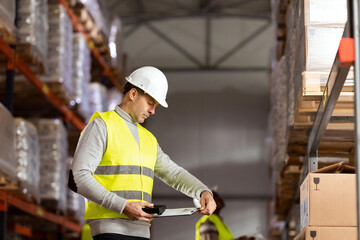 Portrait of a man working in warehouses. She is wearing protective workwear and holding a clipboard and barcode reader.