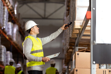 Portrait of a man working in warehouses. She is wearing protective workwear and holding a clipboard and barcode reader.