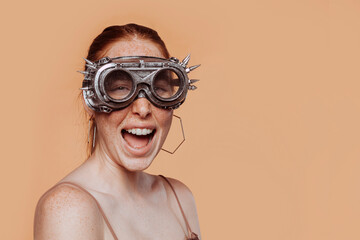 Young happy smiling red-haired woman with freckles in glamourous steam punk googles, studio...
