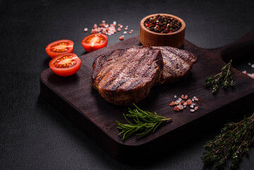 Delicious fresh juicy beef steak with spices and herbs on a dark concrete background
