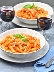 Plate of All'Arrabbiata penne and glasses of red wine. Vertical shot from a high angle of view.