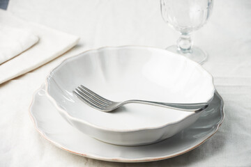 An empty plate with a fork and an empty wine glass on a table with a linen tablecloth. High angle...