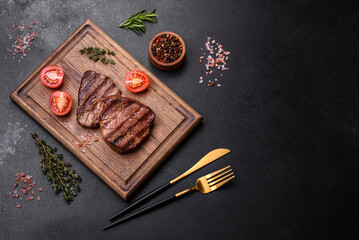 Delicious fresh juicy beef steak with spices and herbs on a dark concrete background