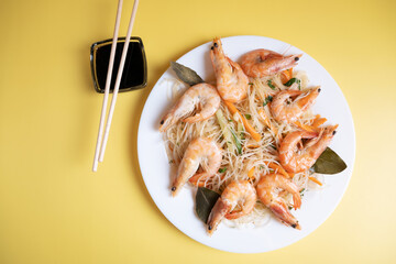 Funchosa salad with shrimp and soy sauce on a yellow background