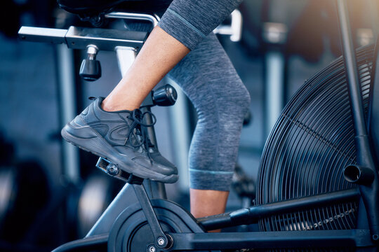 Closeup, fitness and person training, bike and exercise for wellness, gym and sneakers. Athlete, healthy female and bicycle for cardio, strong and power for legs workout, health or sports for cycling