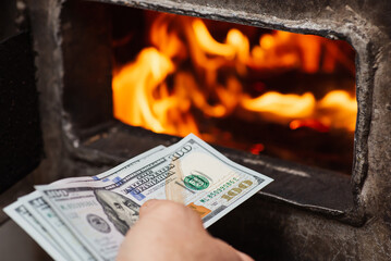 American money in hand of a person near opened door of solid fuel boiler, close up. Expensive...