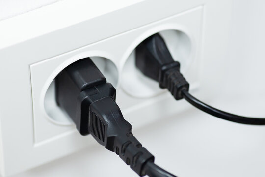 Two electric plugs plugged into an electrical outlet on white wall. Electricity concepts, details of modern life
