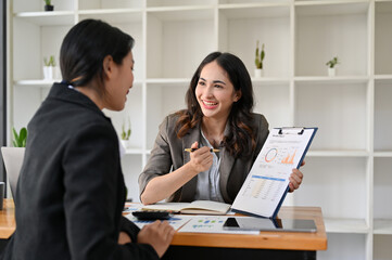 Cheerful Asian businesswoman showing the report to her colleague.
