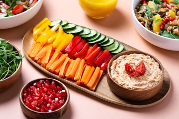 Hummus, vegetables and vegan salads on light beige table top, variety of plates for vegan menu