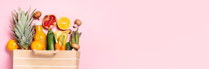 Fresh fruit and vegetables in paper bag on pastel pink background, top view, copy space