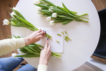 woman trims the roots of flowers so that they stand longer in a vase. How to prolong the life of a...
